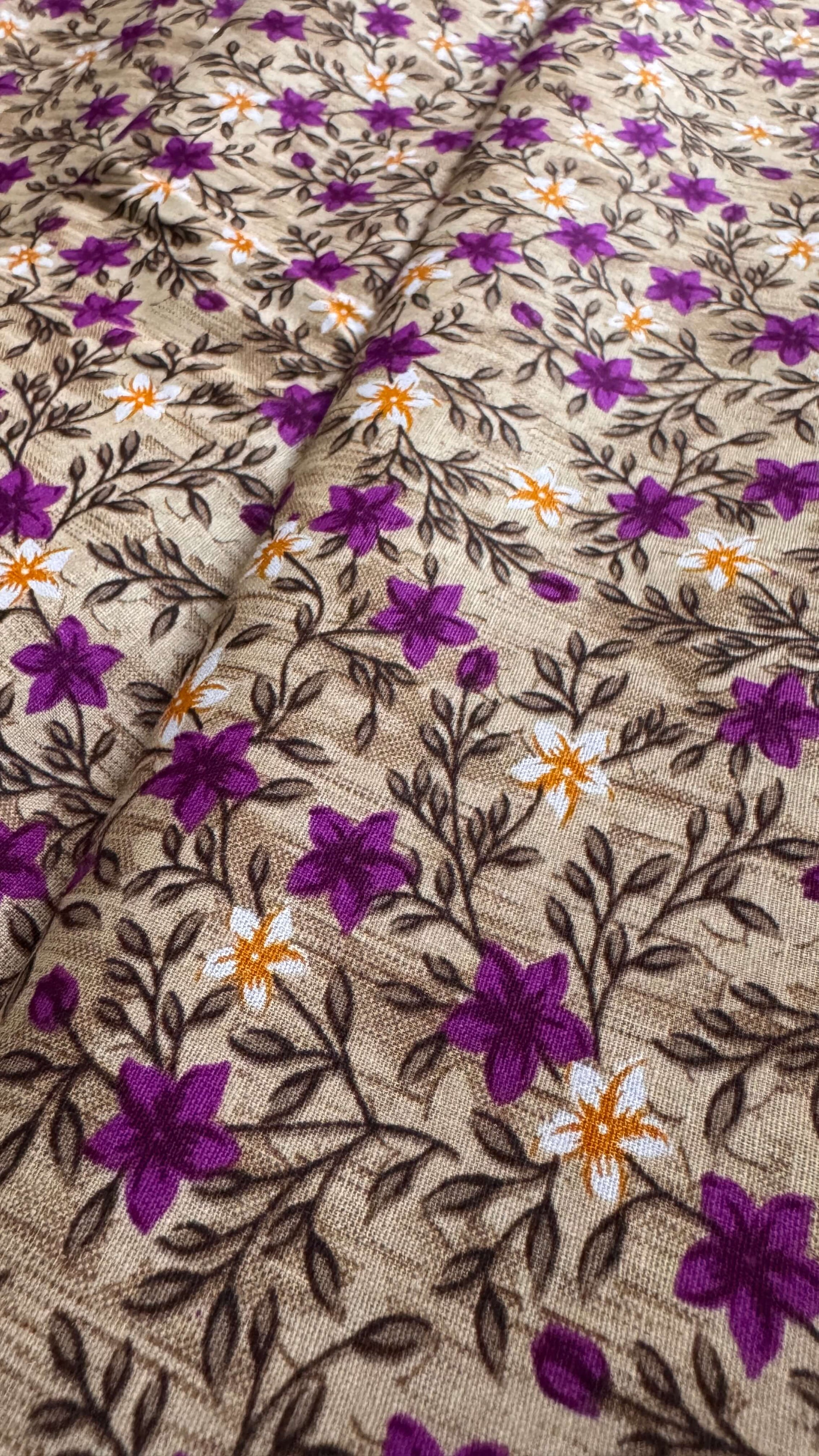 Close-up of fabric with floral pattern featuring purple flowers and brown leaves on a beige background.